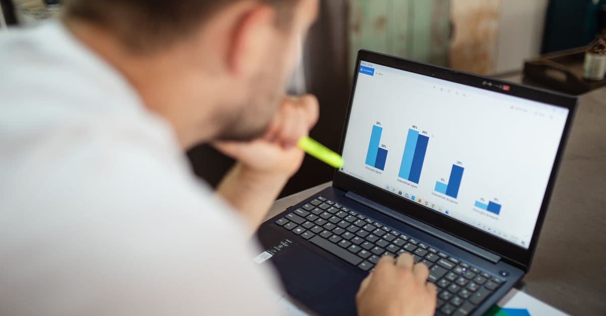 A man with a highlighter in his hand studying a bar chart of survey results on his laptop.
